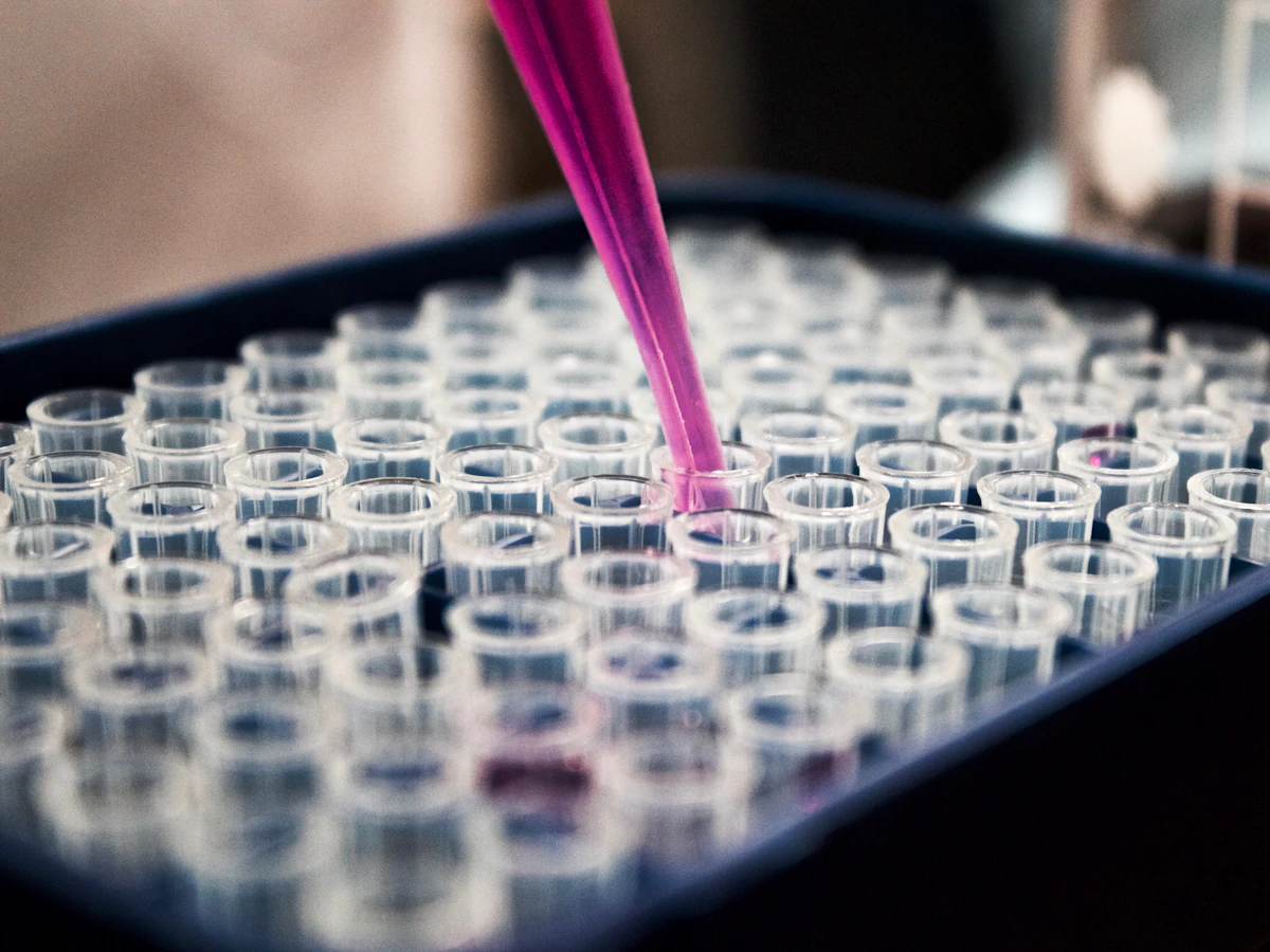 A pipette tip above a rack of clear sample tubes