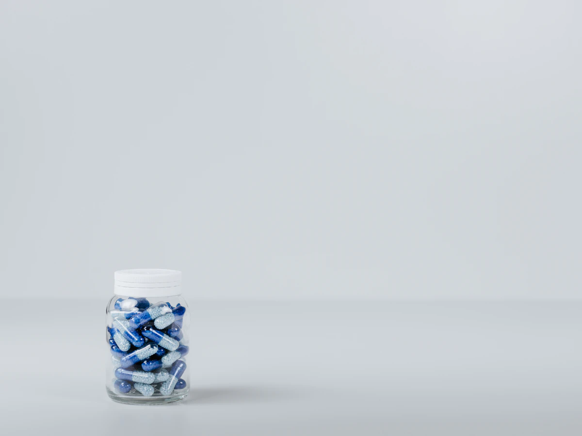 A clear jar of blue and white capsules on a pale grey surface